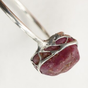 May include: A silver ring with a large, faceted, dark red ruby set in a cage-like design.