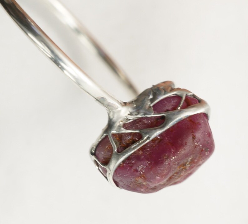 May include: A silver ring with a large, faceted, dark red ruby set in a cage-like design.