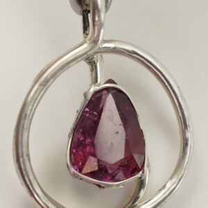 May include: A silver pendant featuring a pink gemstone set within a circular frame. The pendant is crafted with a twisted silver band.