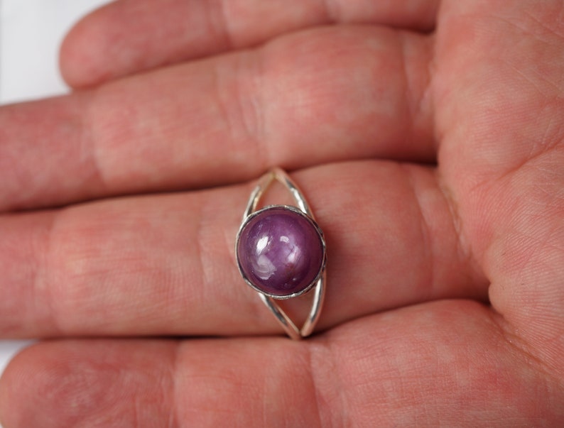 May include: A silver ring with a round, purple gemstone set in the center. The ring has a delicate, open design.