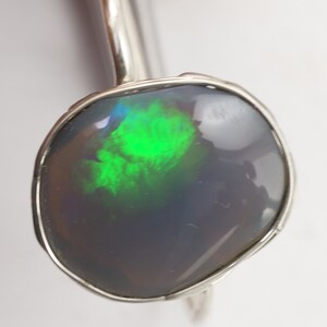 May include: A silver ring with a dark gray opal gemstone that has green and blue flashes of color.