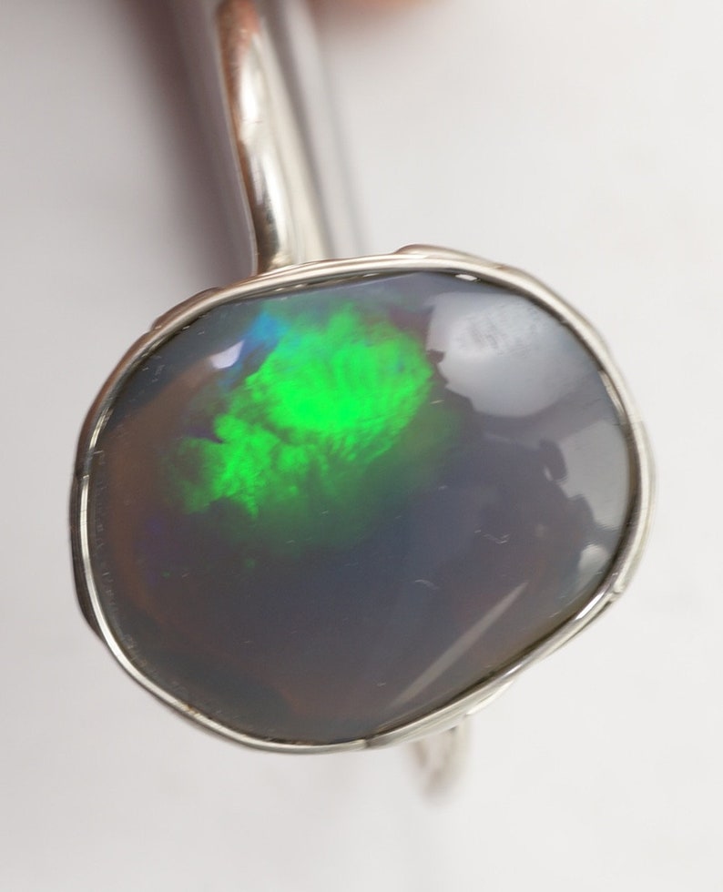 May include: A silver ring with a dark gray opal gemstone that has green and blue flashes of color.