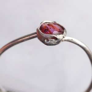 Op de afbeelding: Een zilveren ring met een roze edelsteen in een delicate, organisch gevormde zetting.