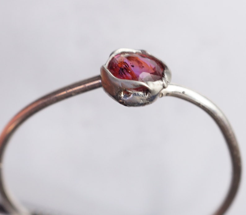 Op de afbeelding: Een zilveren ring met een roze edelsteen in een delicate, organisch gevormde zetting.