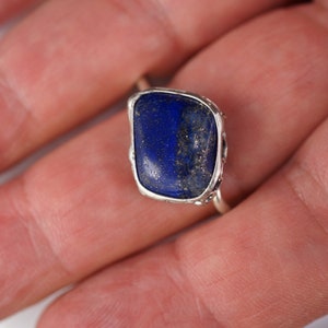 Puede incluir: Un anillo de plata con una gran piedra de lapisl&aacute;zuli azul oscuro engastada en un engaste de bisel. La piedra tiene una forma ligeramente irregular y est&aacute; rodeada por una delicada banda de plata.