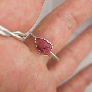 May include: A silver ring with a raw pink ruby gemstone set in the centre.