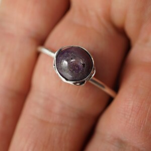 May include: A silver ring with a purple gemstone set in a bezel setting.