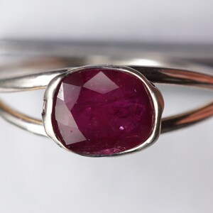 Op de afbeelding: Een zilveren ring met een dieprode robijn-edelsteen gezet in een bezel-setting. De ring heeft een unieke, gedraaide band.