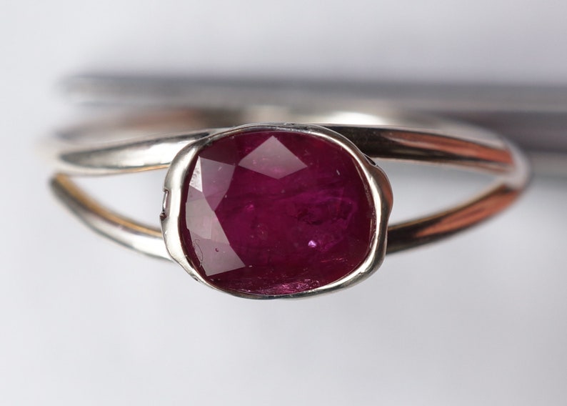 Op de afbeelding: Een zilveren ring met een dieprode robijn-edelsteen gezet in een bezel-setting. De ring heeft een unieke, gedraaide band.