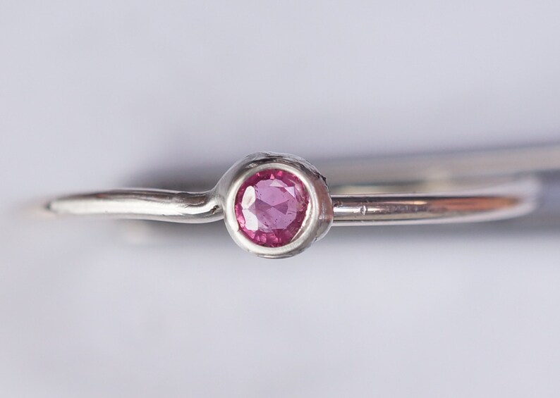 K&ouml;nnte beinhalten: Ein silberner Ring mit einem kleinen, runden, rosafarbenen Edelstein, der in einer strukturierten Fassung sitzt.