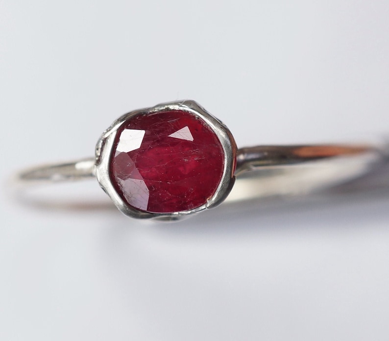 Pode incluir: Um anel de prata com uma gema de rubi vermelho engastada em uma banda texturizada.