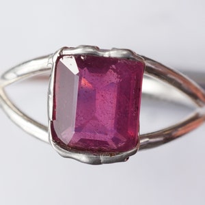 May include: A silver ring with a large, faceted, pink gemstone set in a bezel setting.