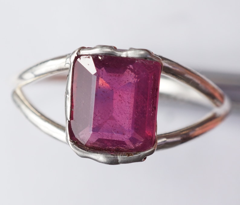 May include: A silver ring with a large, faceted, pink gemstone set in a bezel setting.
