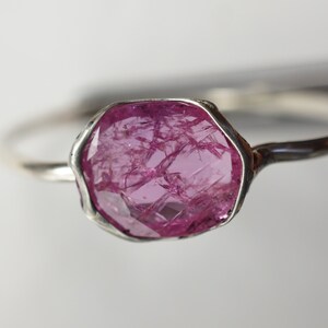 May include: A silver ring with a large, pink, faceted gemstone set in a bezel setting.