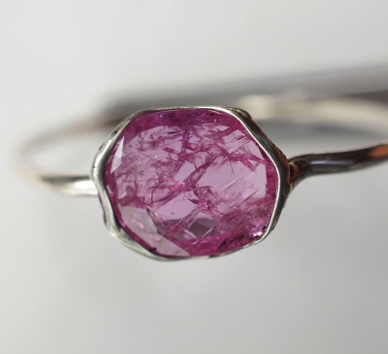 May include: A silver ring with a large, pink, faceted gemstone set in a bezel setting.