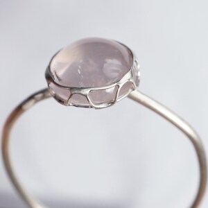 Puede incluir: Un anillo de plata con un delicado dise&ntilde;o de alambre que sostiene una piedra de cuarzo rosa p&aacute;lido.