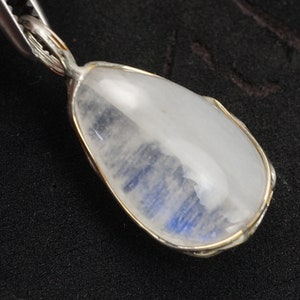 May include: A silver pendant with a teardrop-shaped moonstone. The moonstone is translucent and has a blue sheen.