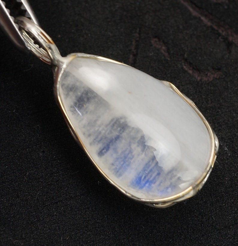 May include: A silver pendant with a teardrop-shaped moonstone. The moonstone is translucent and has a blue sheen.
