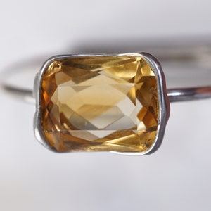 May include: A silver ring with a large, rectangular, faceted, yellow citrine gemstone.