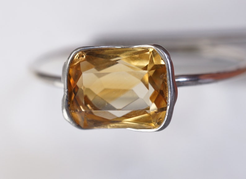 May include: A silver ring with a large, rectangular, faceted, yellow citrine gemstone.