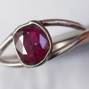 K&ouml;nnte beinhalten: Ein silberner Ring mit einem tief roten, facettierten Edelstein, der in einer Zargenfassung sitzt.