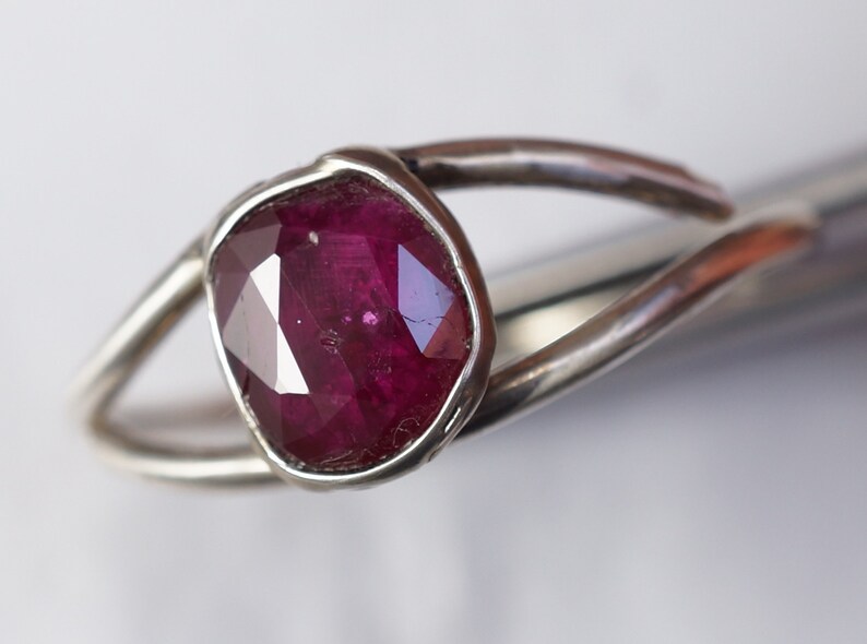 K&ouml;nnte beinhalten: Ein silberner Ring mit einem tief roten, facettierten Edelstein, der in einer Zargenfassung sitzt.