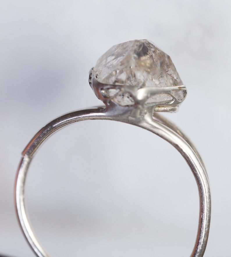 May include: A silver ring with a clear, faceted, raw diamond gemstone set in a delicate, openwork design.