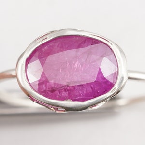 Op de afbeelding: Een zilveren ring met een roze ovale edelsteen gezet in een getextureerde zetting.