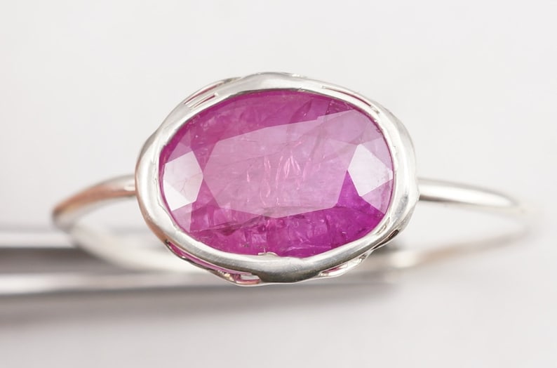 Op de afbeelding: Een zilveren ring met een roze ovale edelsteen gezet in een getextureerde zetting.