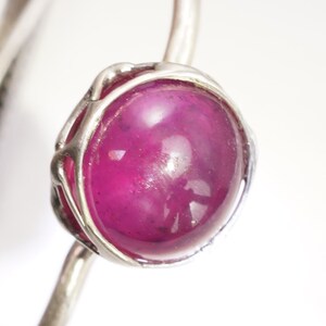 May include: A silver ring with a large, round, cabochon-cut, pink gemstone set in a delicate, wire-wrapped setting.