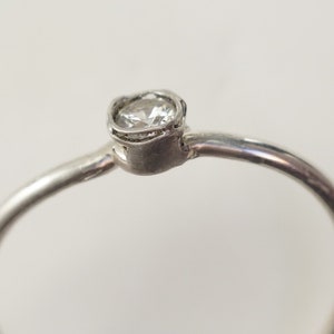 May include: A silver ring with a single round clear stone set in a delicate, textured band.