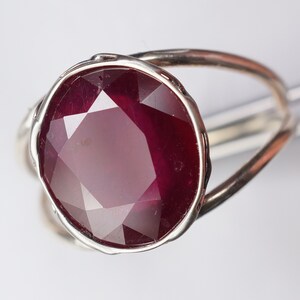 May include: A silver ring with a large, faceted ruby gemstone. The ruby is a deep red color and has a high polish.