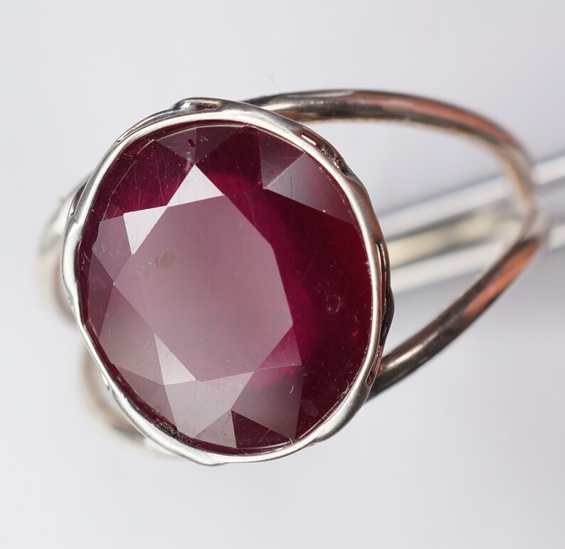 May include: A silver ring with a large, faceted ruby gemstone. The ruby is a deep red color and has a high polish.