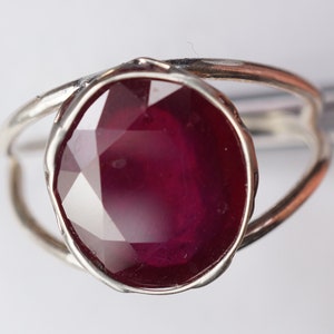 May include: A silver ring with a large, faceted ruby gemstone. The ring has a simple, modern design.