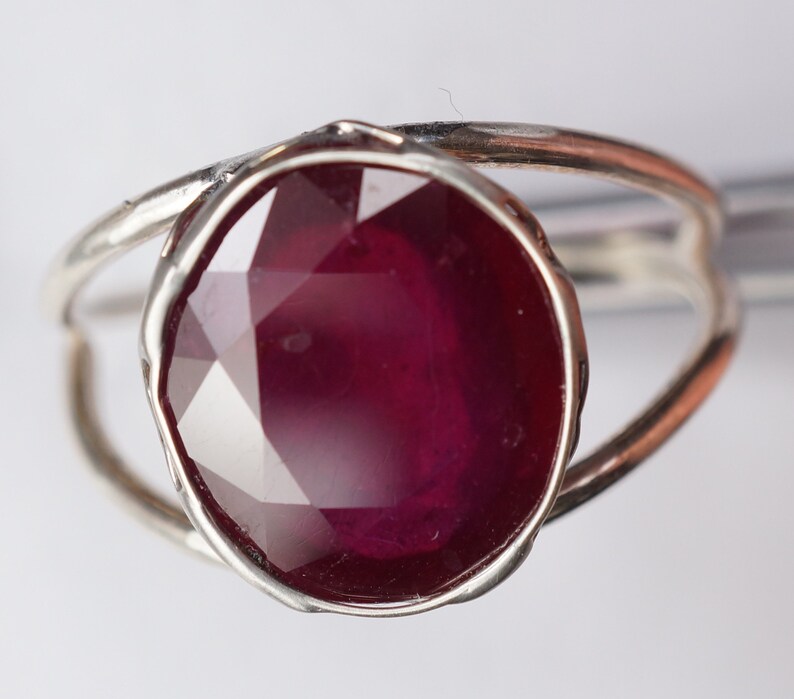 May include: A silver ring with a large, faceted ruby gemstone. The ring has a simple, modern design.