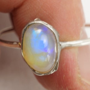 May include: A silver ring with a white opal gemstone. The opal has a blue and purple iridescent sheen.