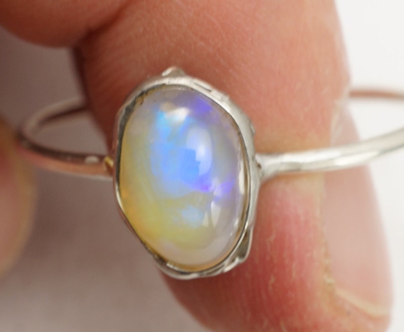 May include: A silver ring with a white opal gemstone. The opal has a blue and purple iridescent sheen.