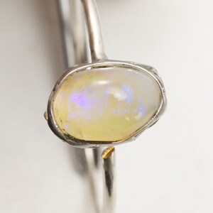 May include: A silver ring with a yellow opal gemstone set in a silver bezel. The ring has a textured band.