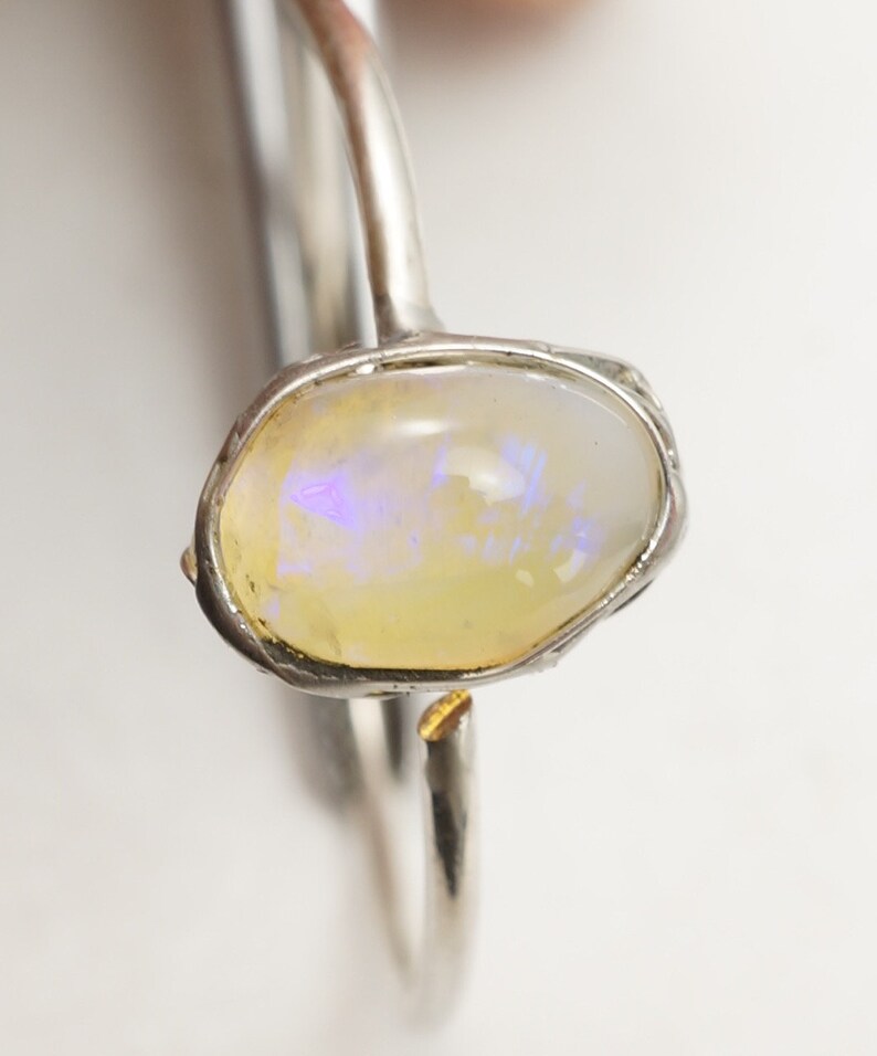 May include: A silver ring with a yellow opal gemstone set in a silver bezel. The ring has a textured band.