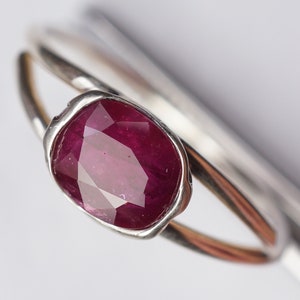 Op de afbeelding: Een zilveren ring met een dieprode robijn-edelsteen gezet in een bezel-setting. De ring is simpel van ontwerp met een gladde band.