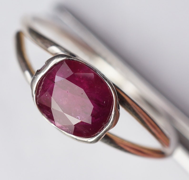 Op de afbeelding: Een zilveren ring met een dieprode robijn-edelsteen gezet in een bezel-setting. De ring is simpel van ontwerp met een gladde band.