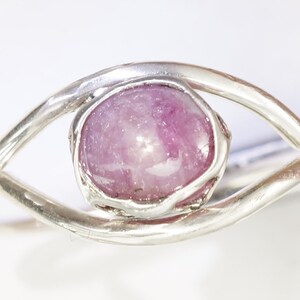 May include: A silver ring featuring a pink gemstone set in a delicate eye-shaped design.