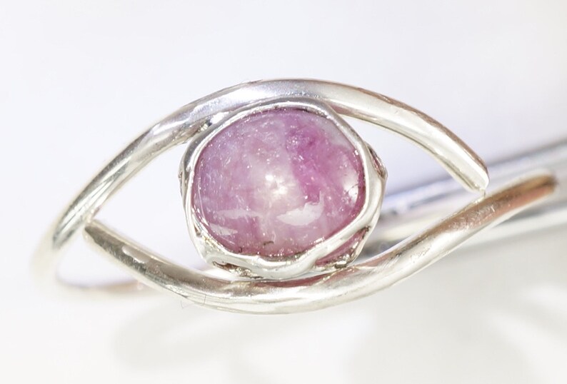 May include: A silver ring featuring a pink gemstone set in a delicate eye-shaped design.