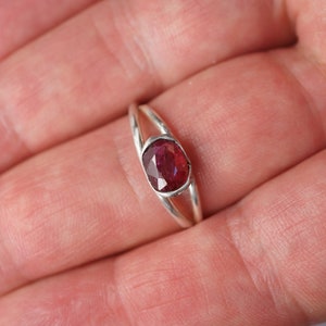 Puede incluir: Un anillo de plata con una piedra ovalada de color rojo oscuro engastada en el centro.