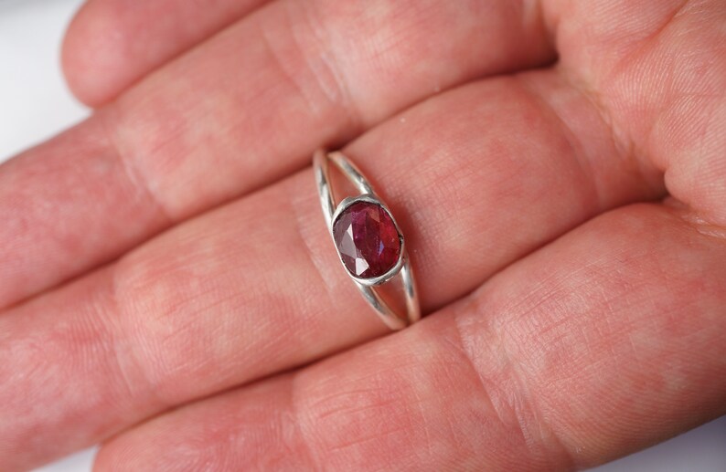 Puede incluir: Un anillo de plata con una piedra ovalada de color rojo oscuro engastada en el centro.