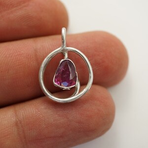 May include: A silver pendant featuring a pink gemstone set within a circular design.