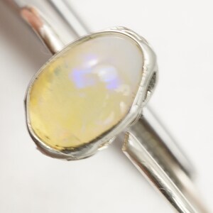May include: A silver ring with a yellow opal gemstone set in a bezel setting.