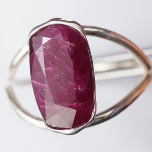 Op de afbeelding: Een zilveren ring met een grote, gefacetteerde robijn. De robijn is diep rood van kleur en heeft een licht onregelmatige vorm.