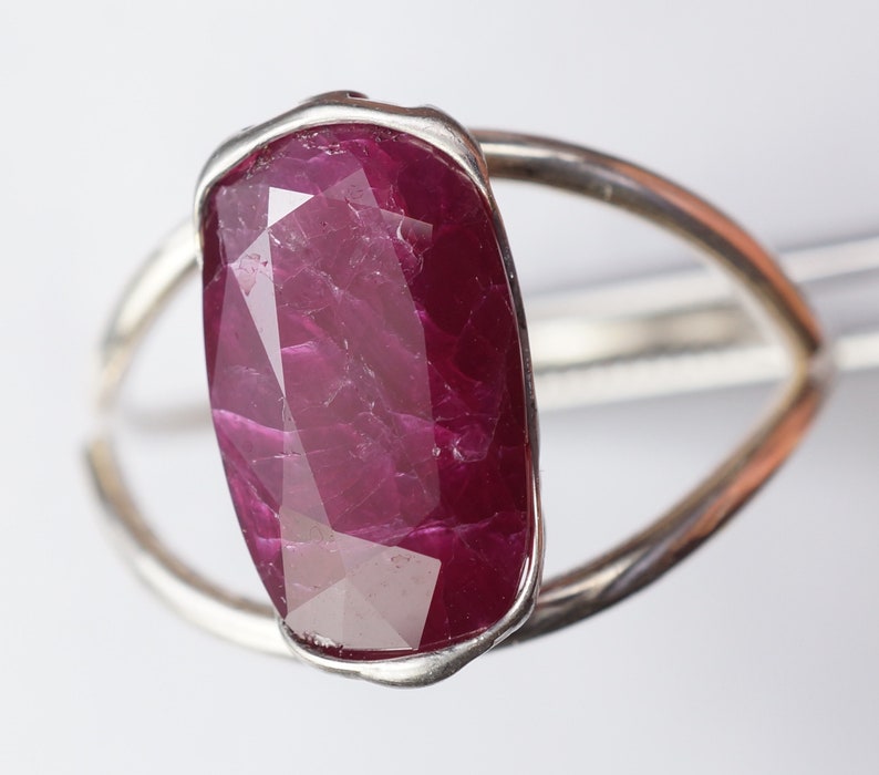 Op de afbeelding: Een zilveren ring met een grote, gefacetteerde robijn. De robijn is diep rood van kleur en heeft een licht onregelmatige vorm.