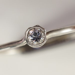 May include: A silver ring with a single round diamond set in a bezel setting.